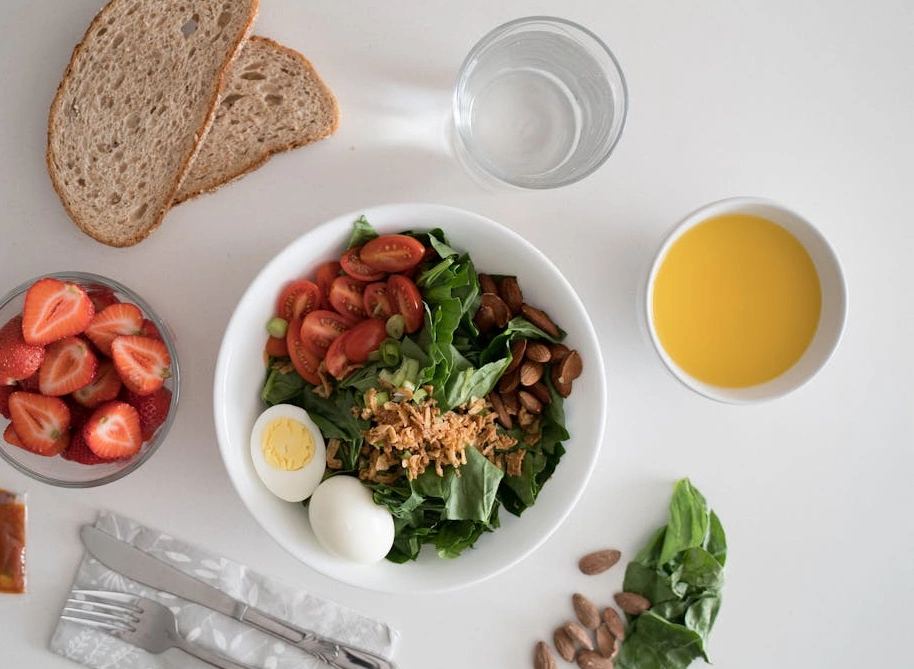 Healthy breakfast with salad, boiled eggs, almonds, whole grain bread, fresh strawberries, and orange juice.