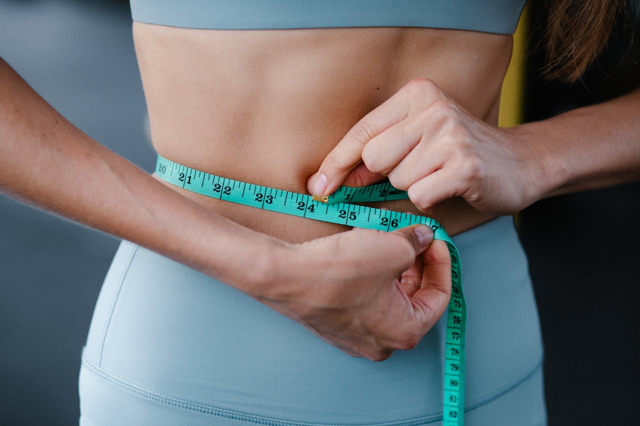Close-up of person in blue workout clothes measuring waist with green tape, related to GLP-1 weight loss patches.