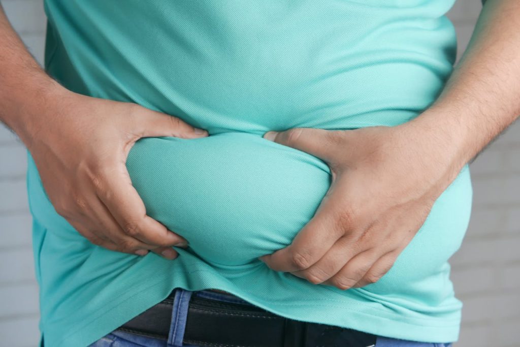 Man holding belly fat showing Ozempic weight loss plateau and causes of slow results in 2025.
