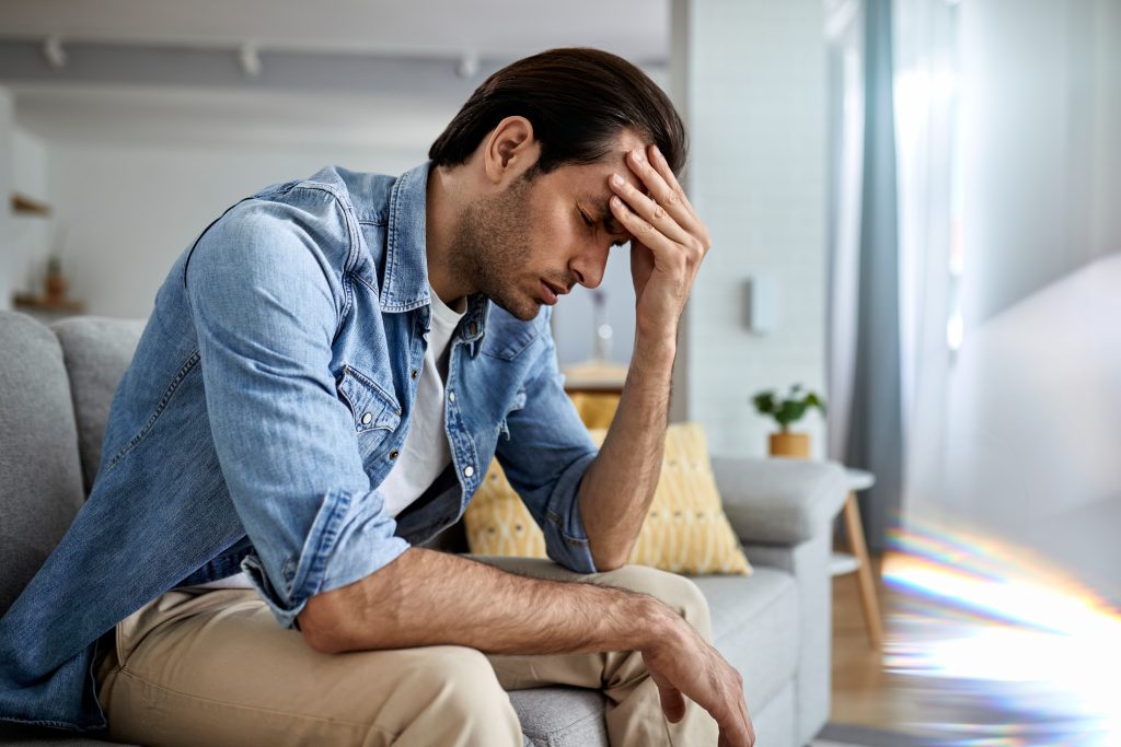 Young man holding his head in stress on a sofa, illustrating how stress can raise blood sugar in Type 2 diabetes.