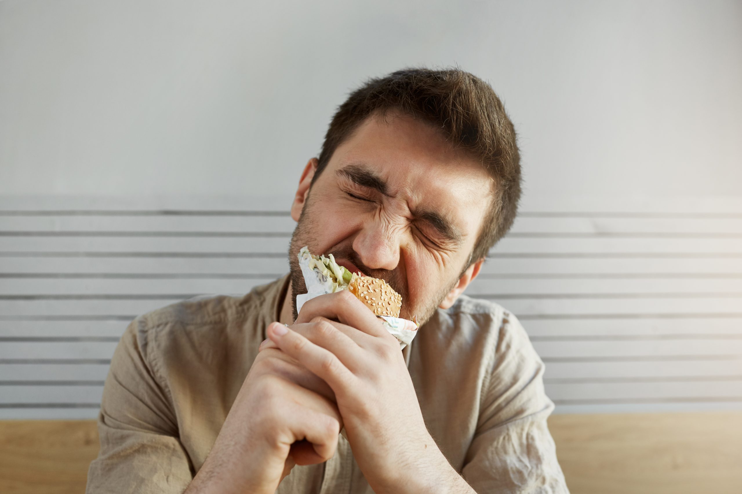 A young man enjoying a sandwich with eyes closed, illustrating how insulin can influence hunger and appetite.