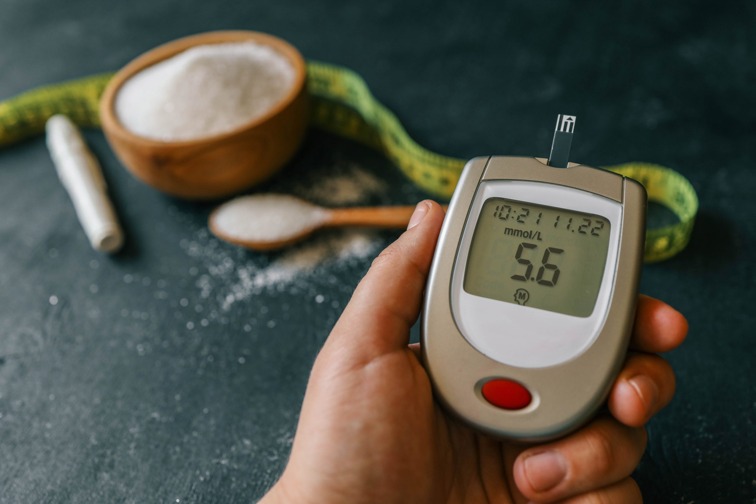 A person holding a digital blood sugar meter over a black table, illustrating the postprandial blood sugar test and its importance.